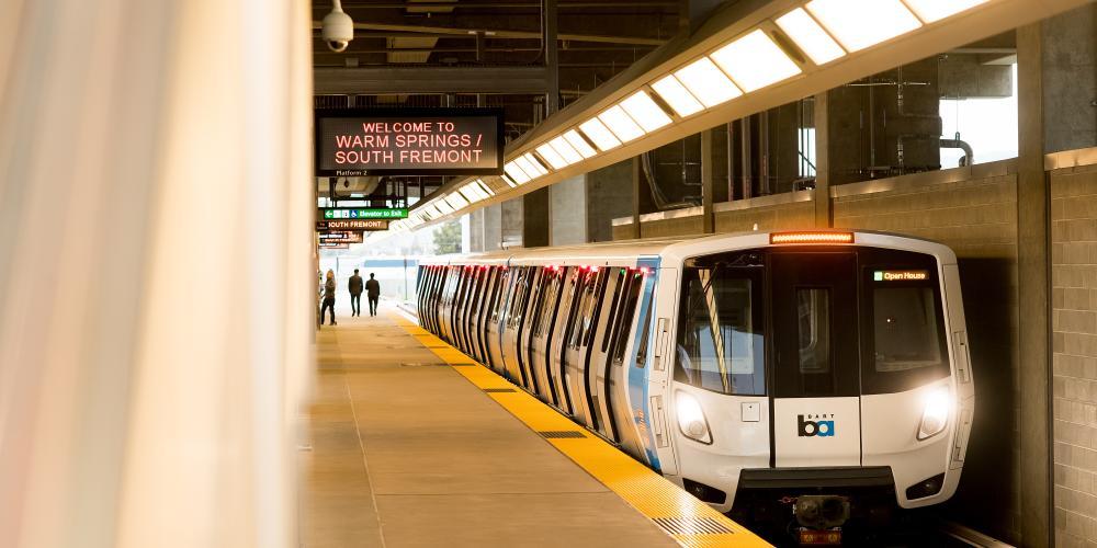 The front of a BART train and a sign that reads WELCOME TO WARM SPRINGS / SOUTH FREMONT, inside a BART station.