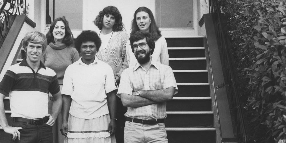 Six people, two men and four women, stand on steps.