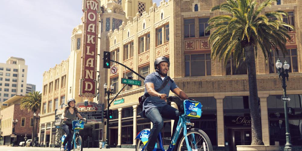 Bicyclists on Ford GoBikes ride past the Fox Theater in Oakland's Uptown district.
