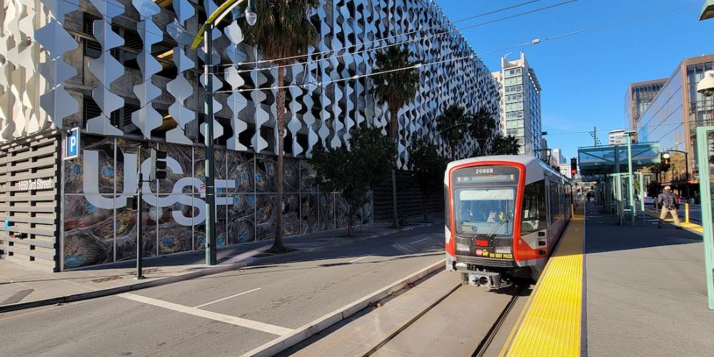 A Muni light rail train at a stop across the street from a UCSF building