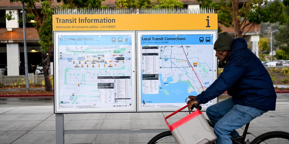 A cyclist rides past a new Transit Information sign at El Cerrito del Norte BART station.