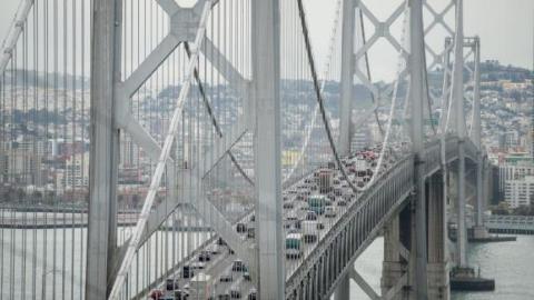 Cars travel west toward San Francisco on the upper deck of the Bay Bridge while SF's cityscape is in the background
