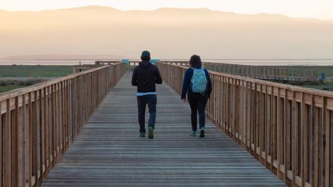 Two people walking down a Bay Trail boardwalk at sunset.